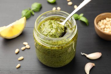 Siyah ahşap masada, kavanozdan kaşıkla taze pesto sosu alıp yakın plan çekiyoruz.
