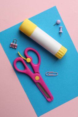 Yapıştırıcı, makas ve pembe zemin üzerinde mavi kağıt, düz yatar