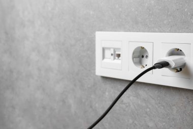Gri duvardaki elektrik prizine bağlı USB adaptörü, yakın plan. Metin için boşluk