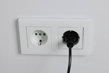 Power plug in socket on white wall, closeup