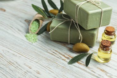 Natural soap bars with olives, sea salt, oil and green leaves on white wooden table, closeup. Space for text