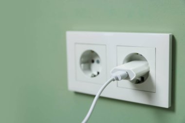 USB adapter with cable plugged into electric socket on green wall, closeup. Space for text