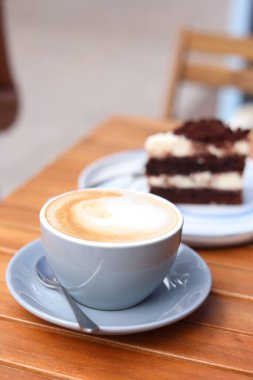 Bir fincan aromatik kahve ve bir dilim kek ahşap masada, yakın plan.