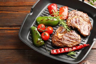 Pan with grilled beef steaks, rosemary and vegetables on wooden table, above view