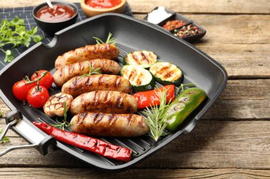 Tavada ızgara sosis, sebze, baharat ve soslar ahşap masada, yakın plan.