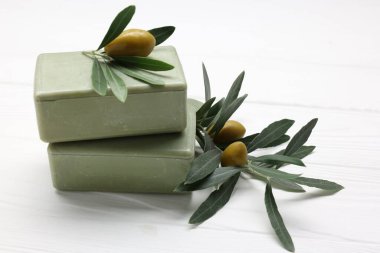 Beyaz ahşap masada el yapımı sabunlar, zeytinler ve yeşil yapraklar, yakın plan.