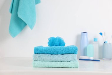 Stack of fresh terry towels and sponge on white table in bathroom