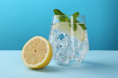 Refreshing water with lemon, mint and ice on table against blue background
