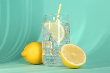Refreshing lemon water with ice in glass and fresh citrus fruits on turquoise background, closeup
