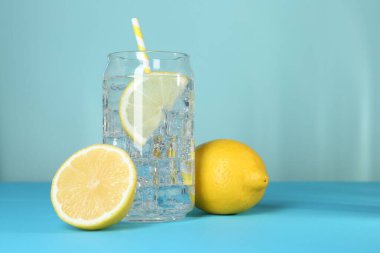 Refreshing lemon water with ice in glass and fresh citrus fruits on light blue background, closeup. Space for text