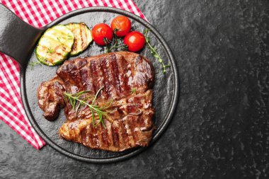 Delicious grilled beef steak with rosemary, zucchini and tomatoes on dark textured table, top view. Space for text