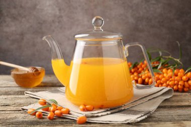 Sea buckthorn tea in glass teapot, honey and fresh berries on wooden table, closeup