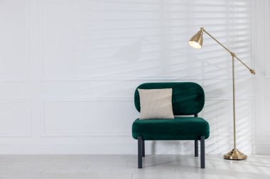 Stylish lamp and comfortable armchair near white wall indoors. Space for text