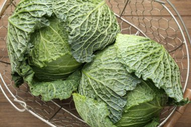 Fresh Savoy cabbages in metal basket on wooden table, top view