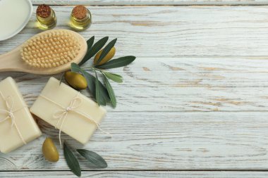 Natural soap bars with olives, brush, oil and green leaves on white wooden table, flat lay. Space for text