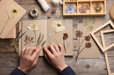 Ahşap masa, üst manzara, kuru çiçekleri deftere koyan kadın.