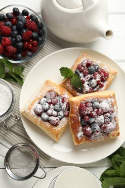 Böğürtlenli poğaça, pudra şekeri ve beyaz ahşap masada nane şekeri, düz uzanmış.