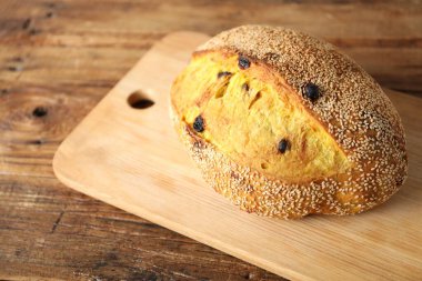 Susam tohumlu bir somun taze ekmek ve ahşap masada kuru üzüm, yakın plan. Metin için boşluk