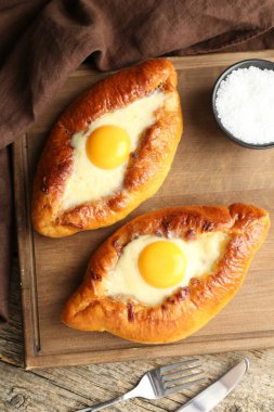 Tasty khachapuris with cheese and eggs served on wooden table, flat lay