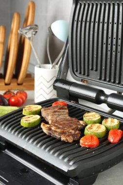 Biftek, kabak ve domatesle açık elektrikli ızgara açık gri masa, yakın plan.