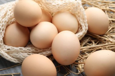 Çiğ tavuk yumurtası, ağ torbası ve saman gri ahşap masa, yakın plan.