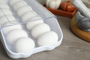 Plastik kabın içinde çiğ tavuk yumurtası ve ahşap tezgahın üzerinde mutfak aletleri, yakın plan.