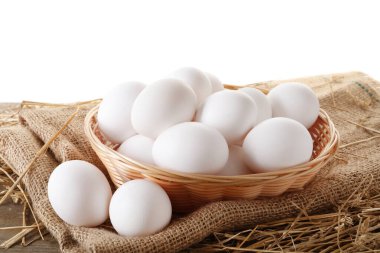 Çiğ tavuk yumurtası, hasır sepet, beyaz arka plana karşı ahşap masa ve saman