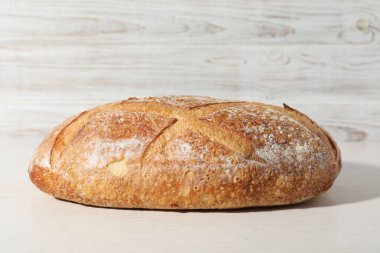 Beyaz ahşap masada bir somun taze ekmek, yakın plan.