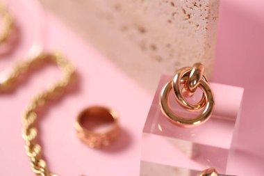 Pembe arka planda altın takıların şık sunumu, yakın plan. Metin için boşluk
