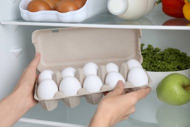 Dolaptan çiğ tavuk yumurtalı yumurta kutusunu alan kadın, yakın plan.