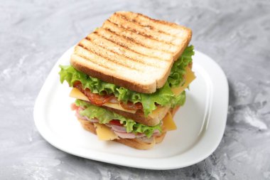 Jambonlu, pastırmalı, peynirli ve sebzeli lezzetli sandviç. Gri desenli masa, yakın plan.