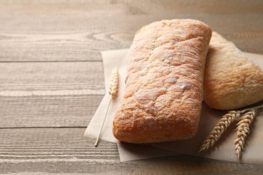 Yeni pişmiş ciabatalar ve ahşap masada buğday kulakları, yakın plan. Metin için boşluk