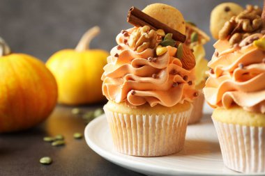 Renkli kremalı, tarçınlı, fındıklı ve sonbahar dekorlu lezzetli kekler gri masada, yakın plan.
