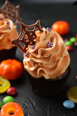 Çikolata ağlı lezzetli kekler ve koyu dokulu masa üzerinde renkli şekerler, yakın plan. Cadılar Bayramı