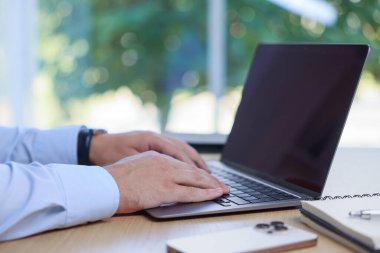 İçerideki ahşap masada dizüstü bilgisayarda çalışan adam, yakın plan.