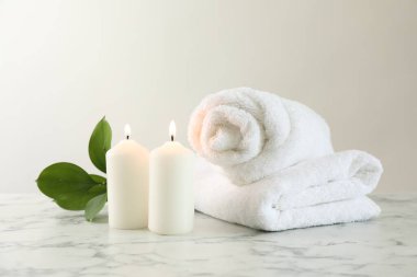 Burning candles, towels and leaves on white marble table, closeup
