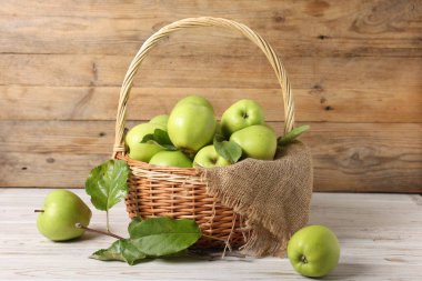 Olgun yeşil elmalarla hasır sepetin içinde beyaz ahşap masada taze yapraklar