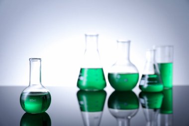 Masada beyaz arka plana karşı yeşil sıvı bulunan farklı bir laboratuar cam.