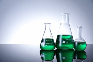 Beyaz zemin üzerinde yeşil sıvı bulunan farklı bir laboratuar cam. Metin için boşluk