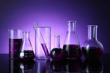 Masada mor arkaplana karşı renk sıvısı bulunan farklı bir laboratuar cam.