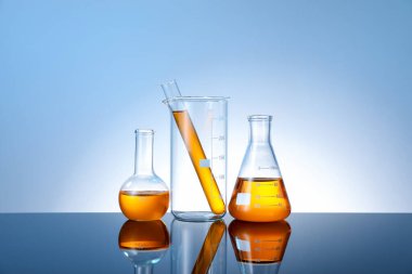 Ayna yüzeyinde turuncu sıvı bulunan farklı cam kaplama açık mavi arkaplan