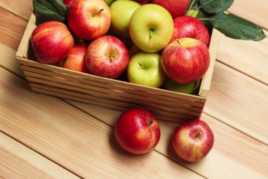 Sandıkta taze elmalar ve ahşap masada yeşil yapraklar.