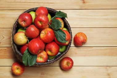 Hasır sepetteki taze elmalar ve ahşap masada yeşil yapraklar, üst manzara. Metin için boşluk