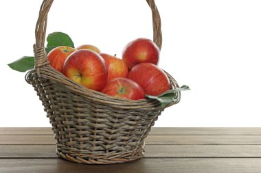 Hasır sepetteki taze elmalar ve beyaz arka plana karşı ahşap masada yeşil yapraklar.