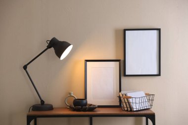 Stylish lamp, other decor and books on console table near beige wall indoors