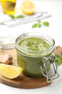 Cam kavanozda lezzetli yeşil pesto ve beyaz ahşap masada malzemeler, yakın plan.
