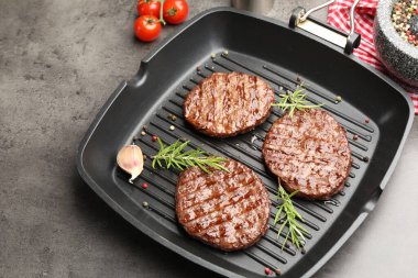 Izgara köfteli tava, domates ve baharatlar gri masada, yakın plan.