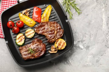 Izgara biftek, mantar, sebze ve baharatlı tava. Gri desenli masa, düz yatak. Metin için boşluk