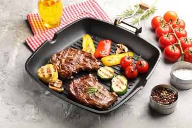 Izgara biftek, mantar, sebze ve baharatlı tava. Gri desenli masa, yakın plan.