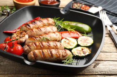 Pan with grilled sausages, vegetables and spices on wooden table, closeup